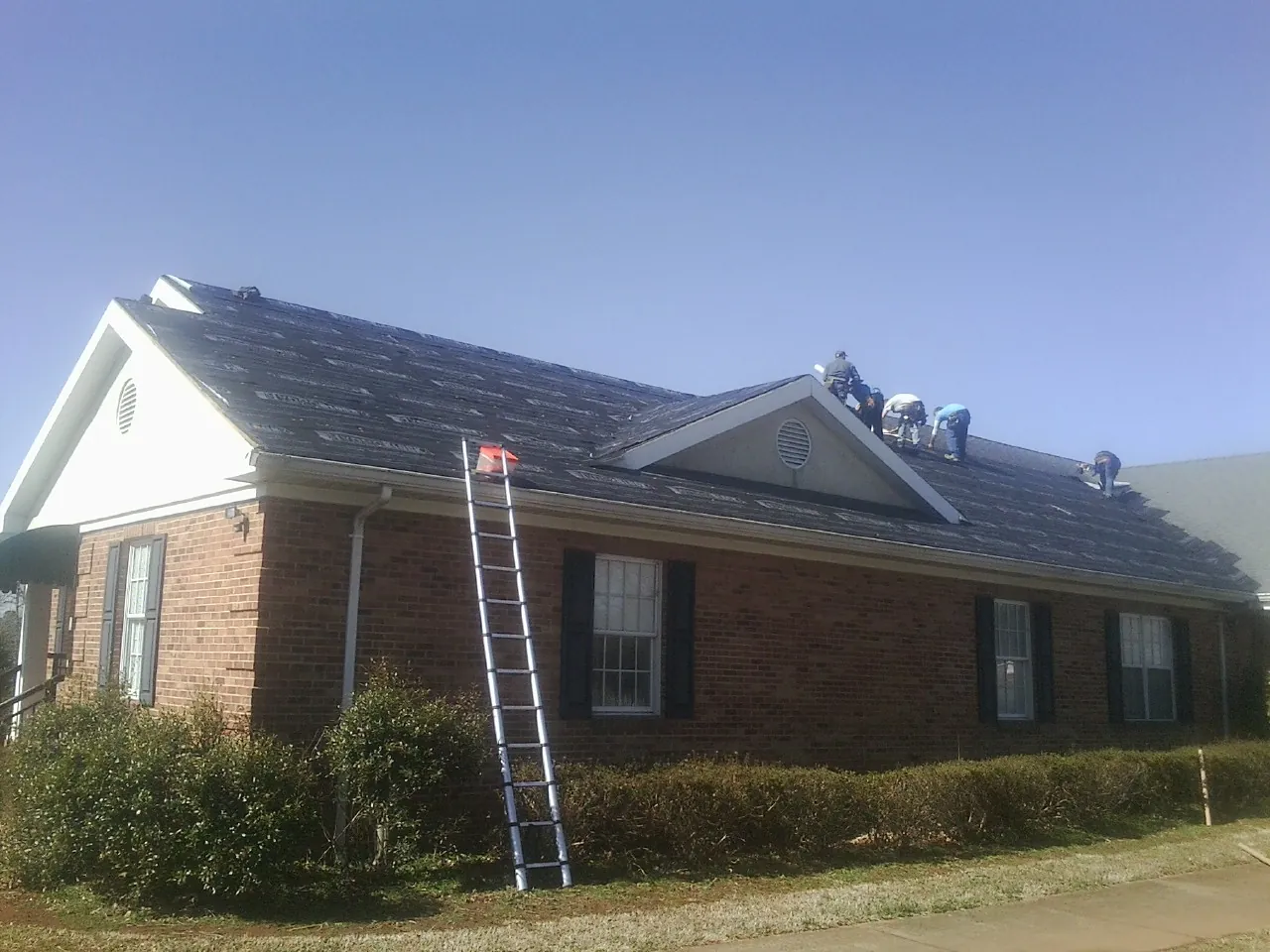 Crew tearing shingles off a brick ranch roof with a ladder set — Emergency Roof Repair work by our crew in Scott Depot