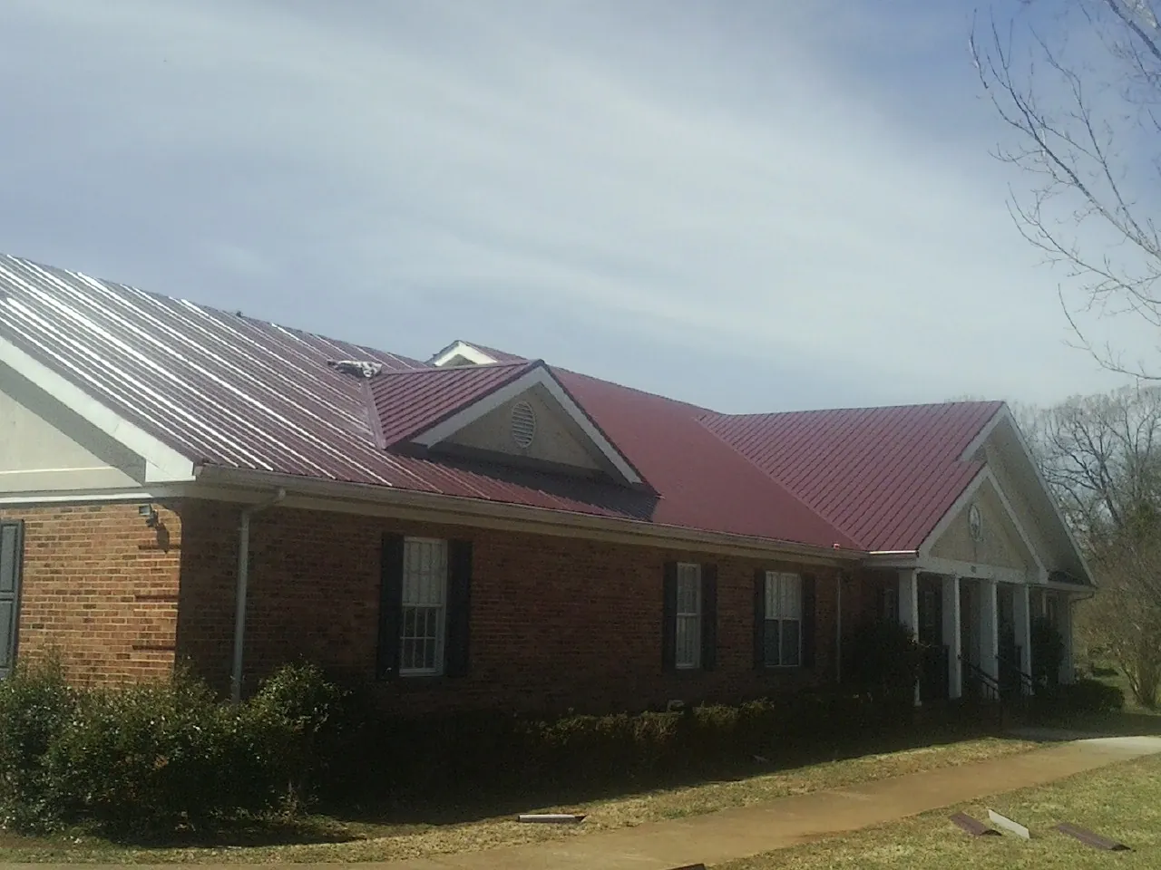 Red metal roof with gabled entries on a long brick building, from a Hail Damage Roof Repair job in Scott Depot