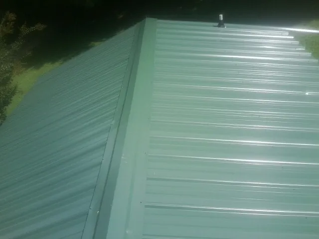 New green metal panels meeting at the ridge of a roof — Flat Roof Repair work by our crew in Scott Depot