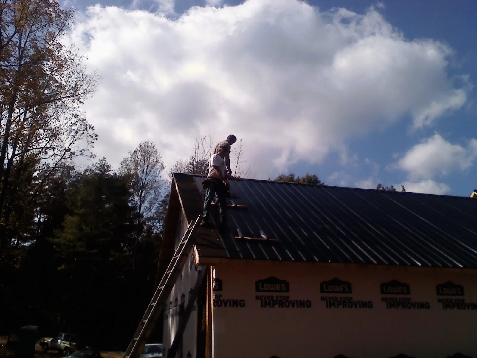 Roofer fastening dark metal panels high against a cloudy sky, from a Roof Inspection job in Scott Depot