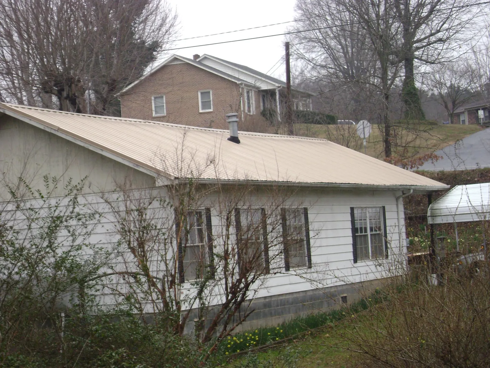 Tan metal roof on a white sided house set into a hillside — Commercial Roofing by Roofing Brothers in Scott Depot